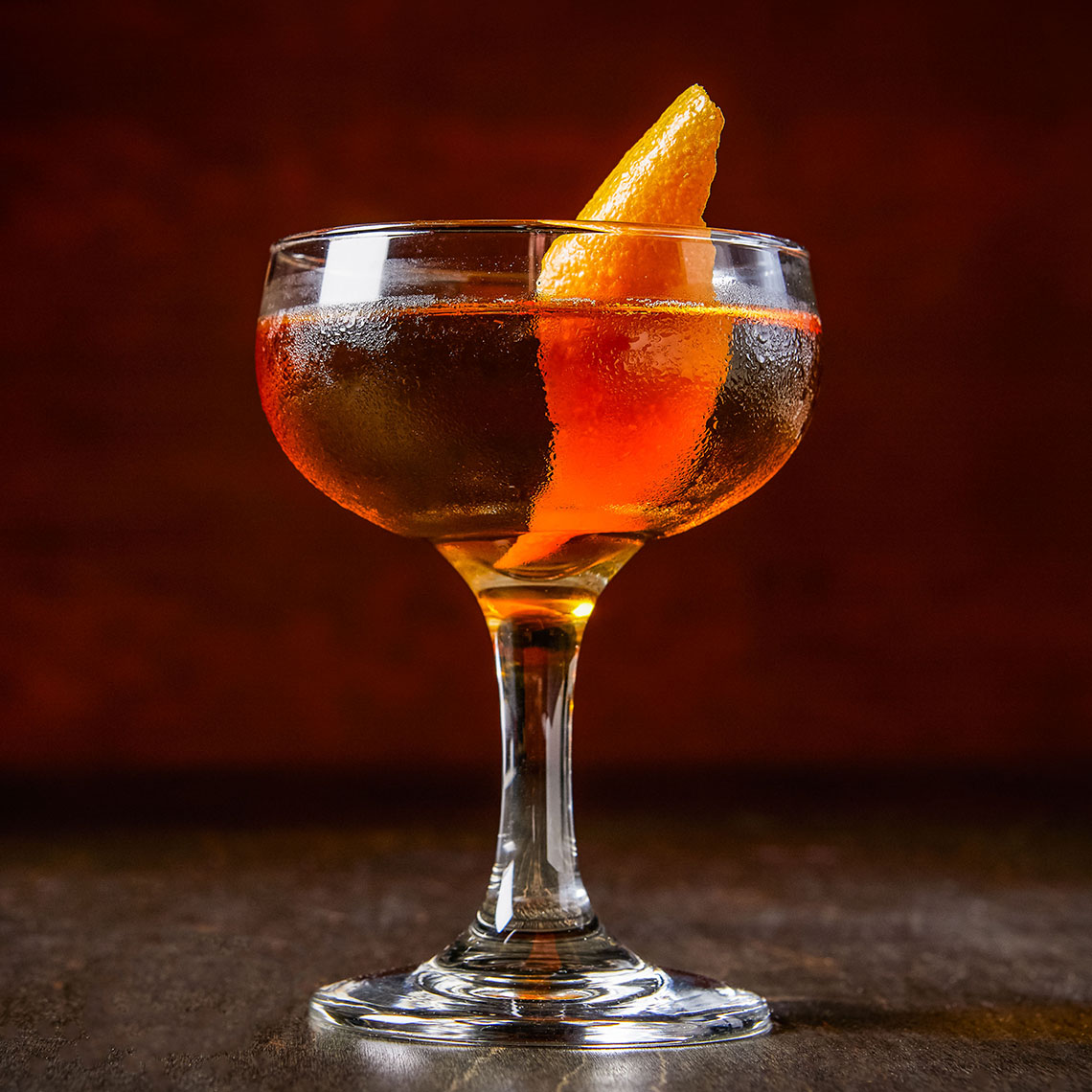 Orange cocktail in a coupe glass with orange peel garnish